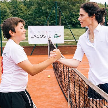 Boy and tennis trainer sharing a high five on a Lacoste Foundation tennis court